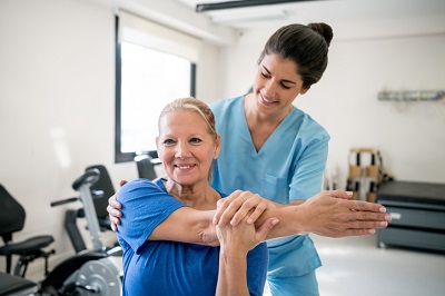 Friendly physical therapist holding senior patient while she stretches her shoulder