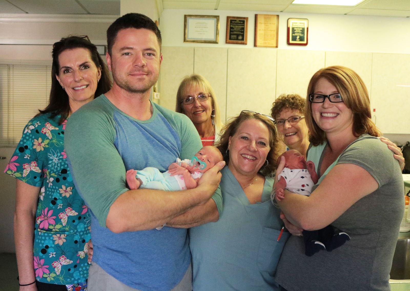 A Father and Mother holding their newborn twins, joined by staff of hospital