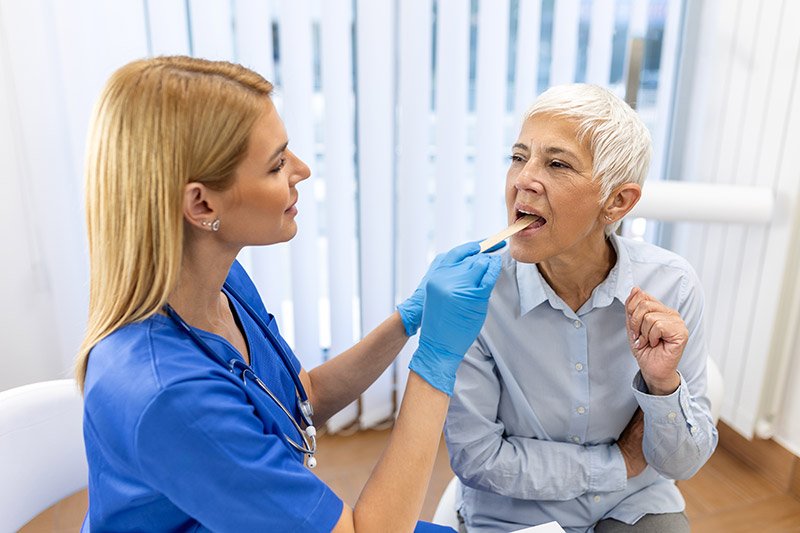 Female nurse in blue scrubs inspecting the tongue of an older woman